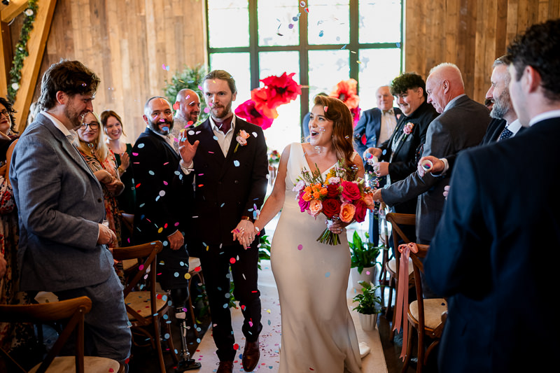 Bride and groom leaving the barn after their wedding ceremony as guests shower them with confetti at Drumhierny Woodland Hideaway, Sligo